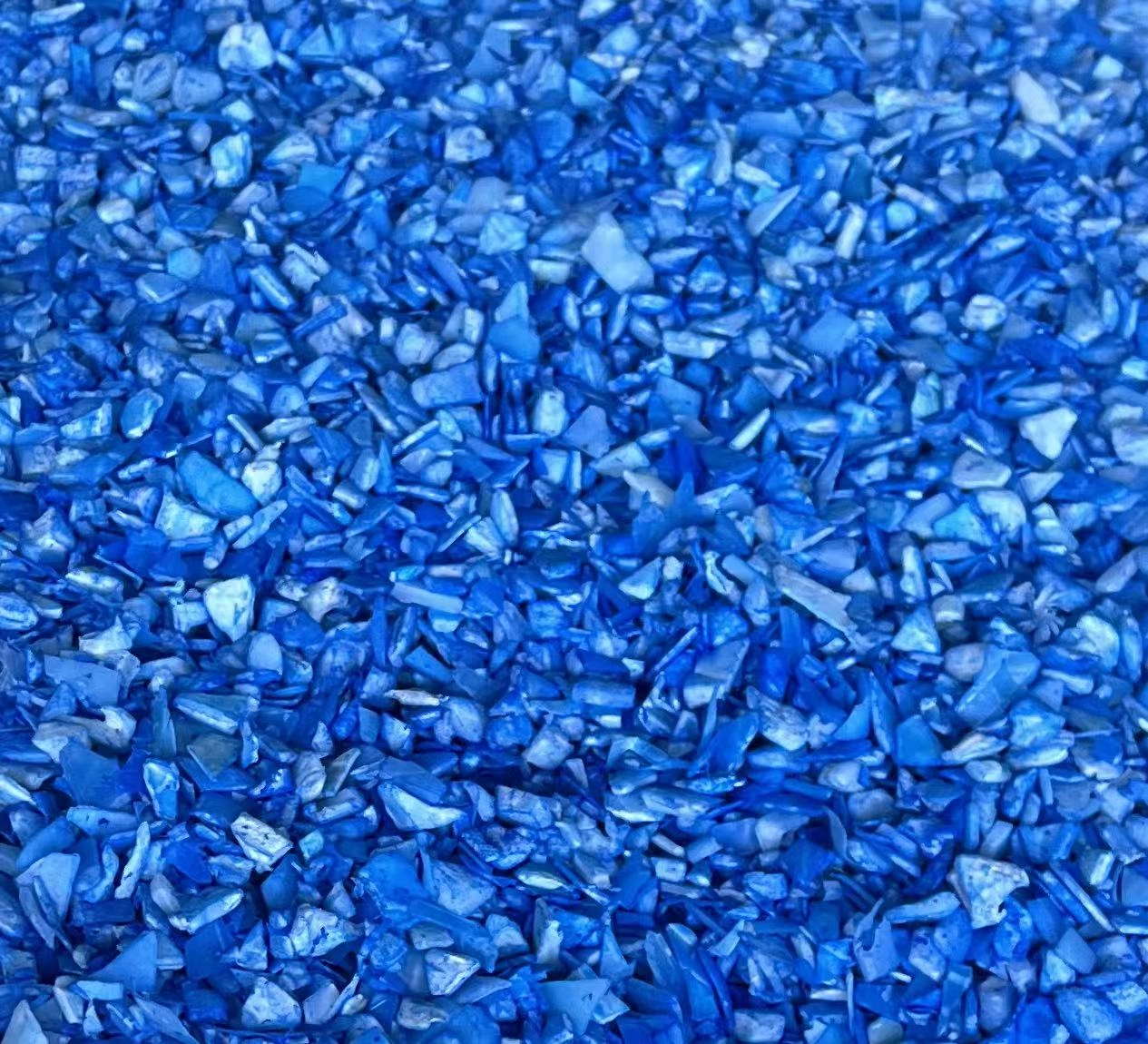 A close-up of small, jagged blue and white recycled plastic pieces - Weihong