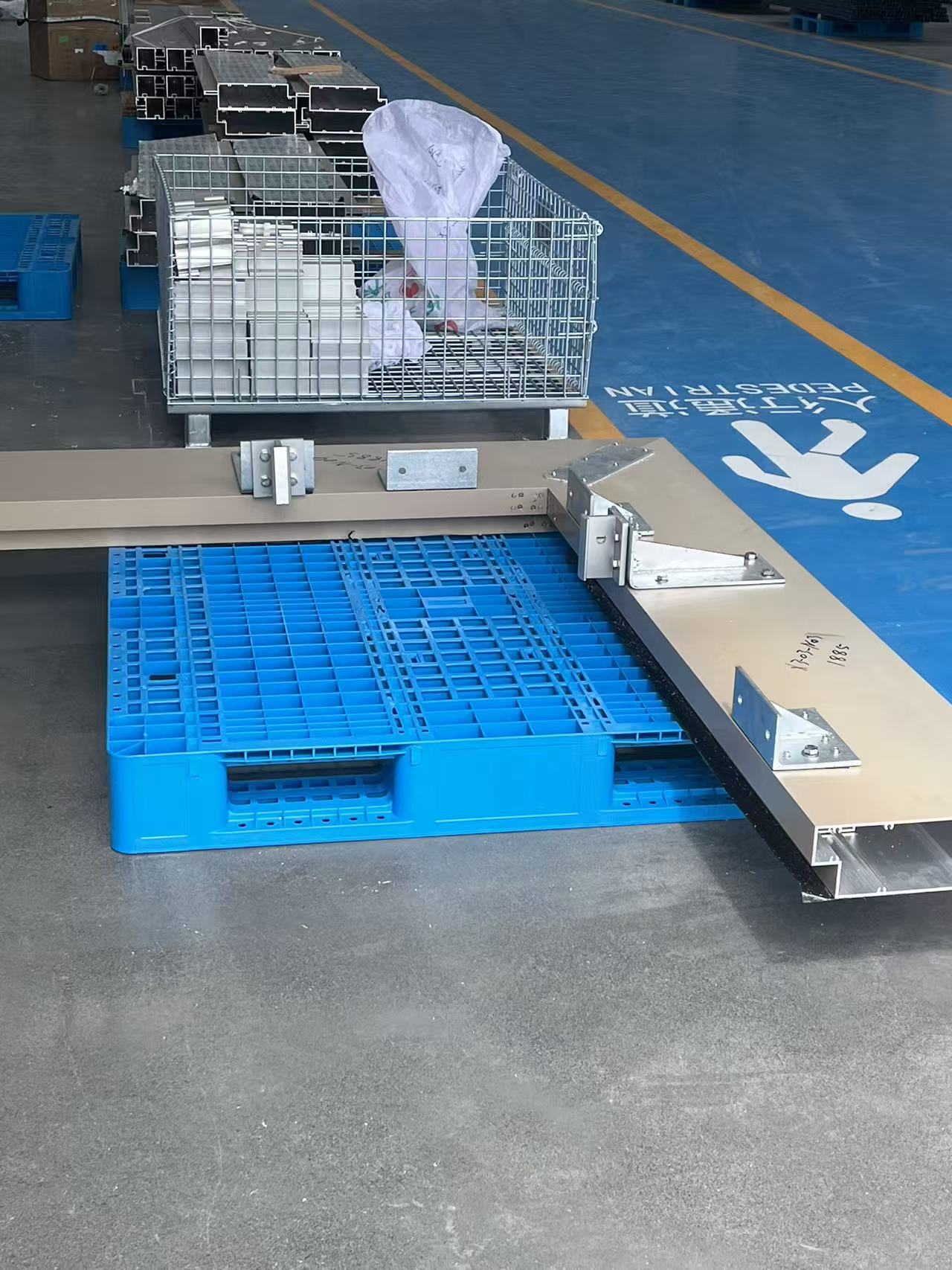 Aluminum components on a blue pallet in a warehouse.