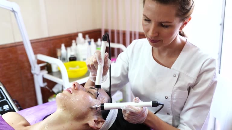 Laser facial photo rejuvenation treatment in progress. A beautician uses a laser device on a client's face.