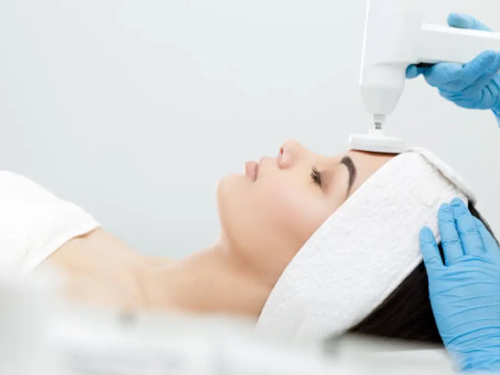 A woman receives a treatment with a laser hair removal machine on her face.