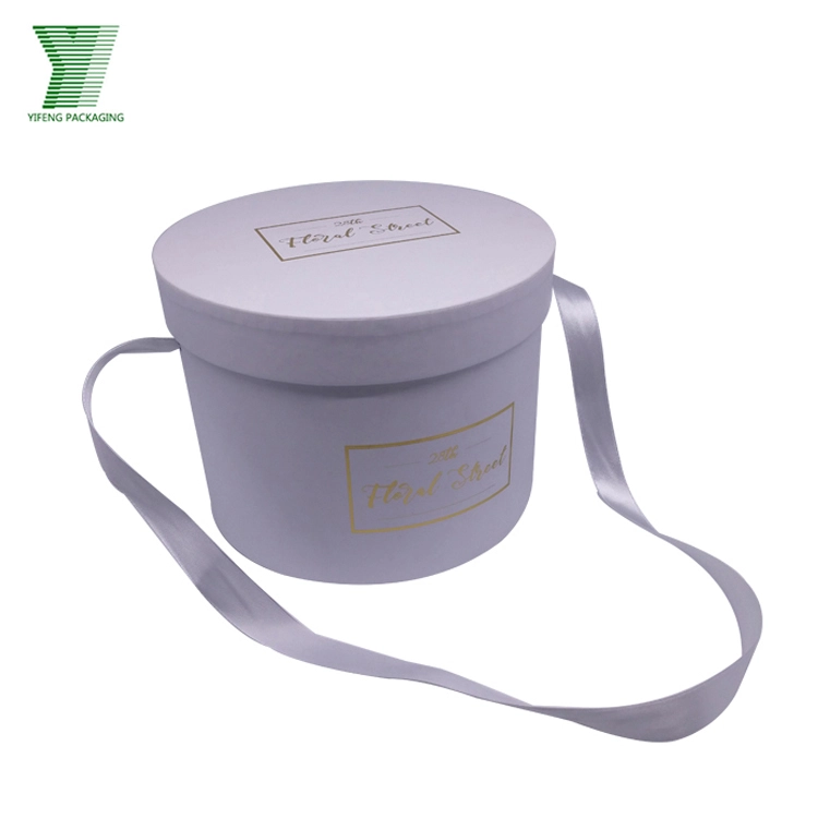 White round gift box with gold logo and lavender ribbon handle. - Yifeng Packaging