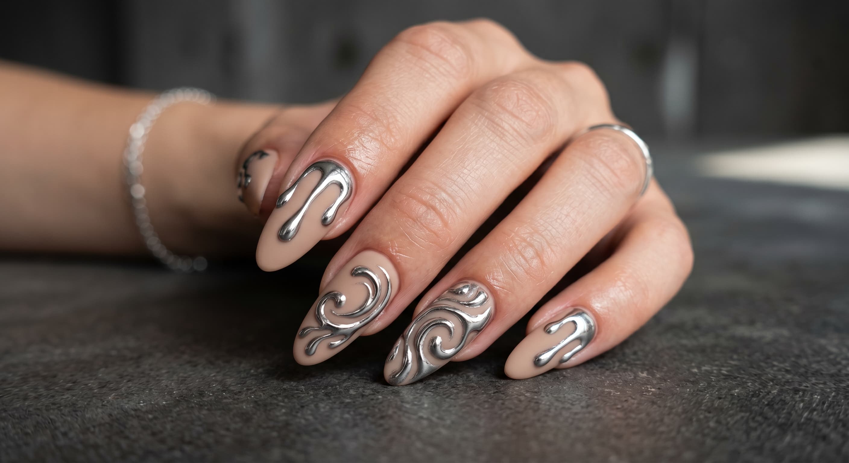 a hand wearing matte black or neutral nude almond press-on nails, featuring raised, 3D metallic silver liquid drips and chrome swirls