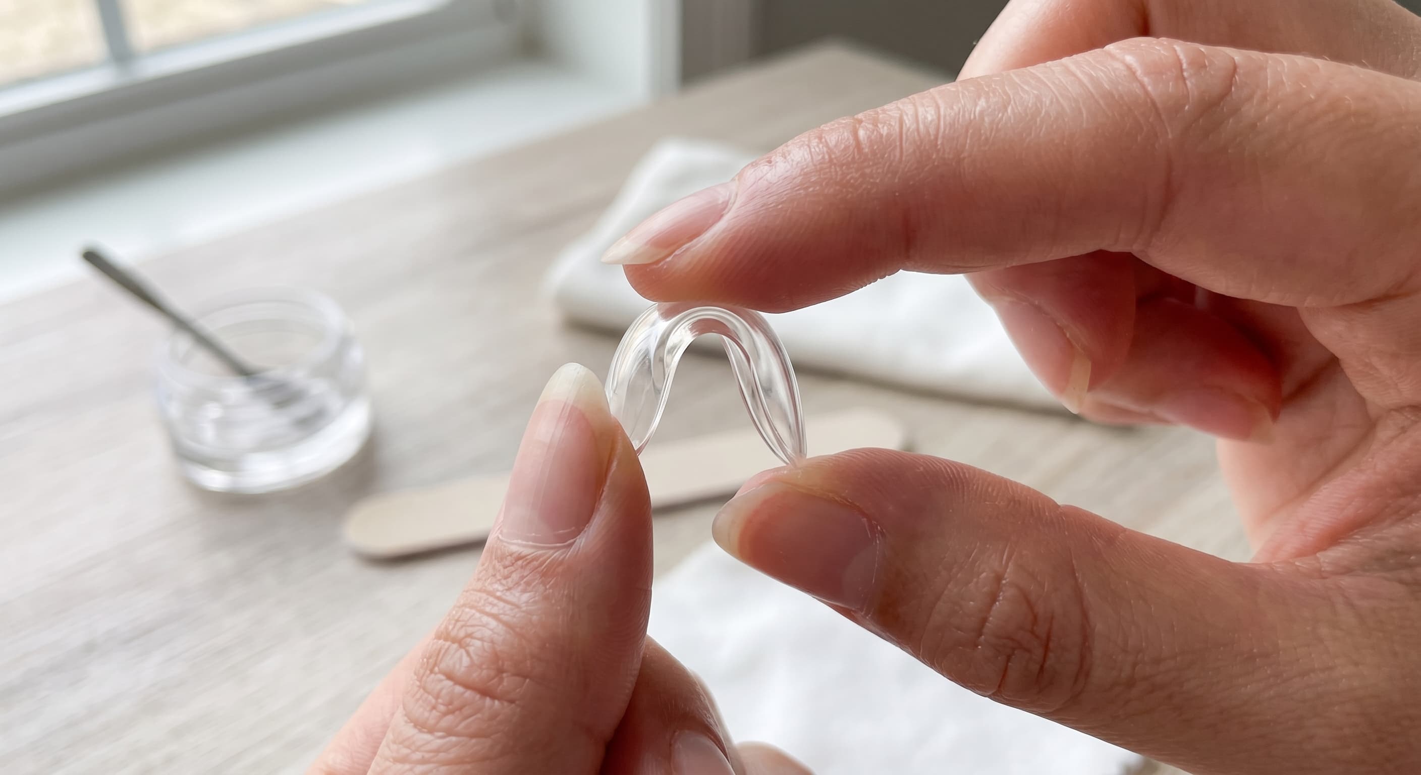 a person bending an unpainted soft gel almond press-on nail between their thumb and index finger